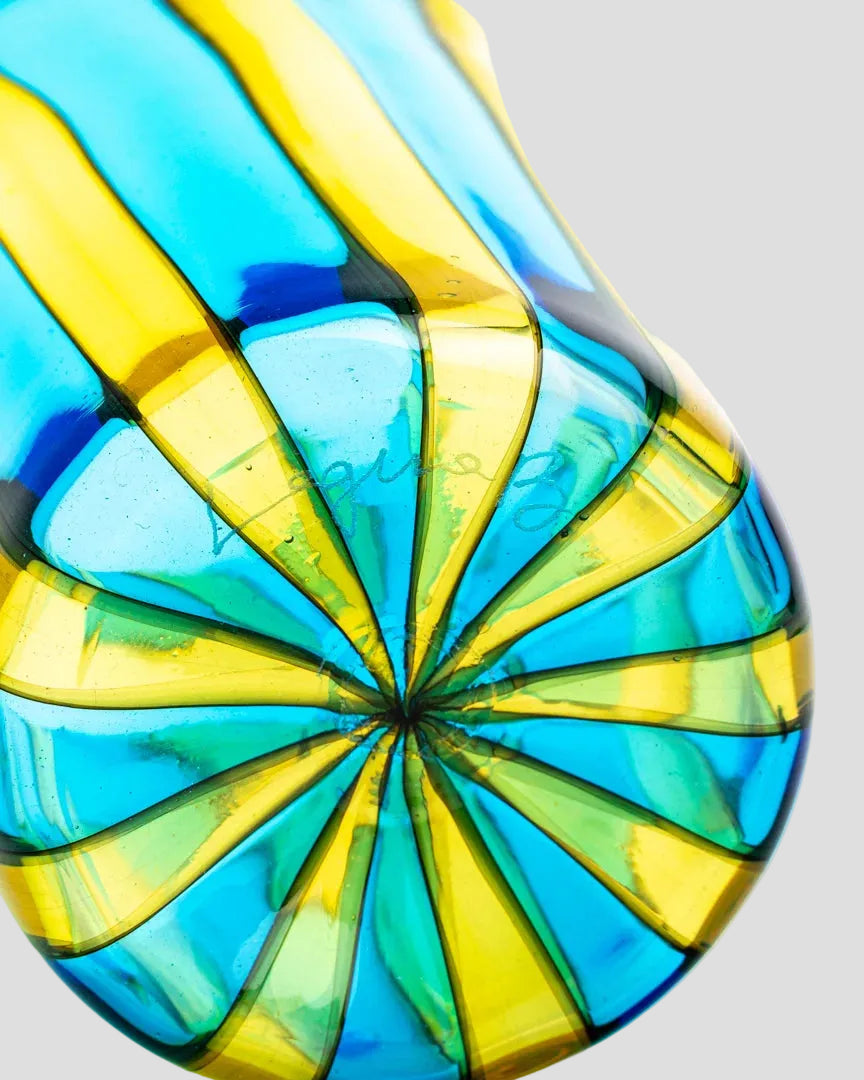 A close-up of a translucent glass vase with vertical fluted ridges and alternating bright blue and yellow-green glass bands, set against a plain white background.