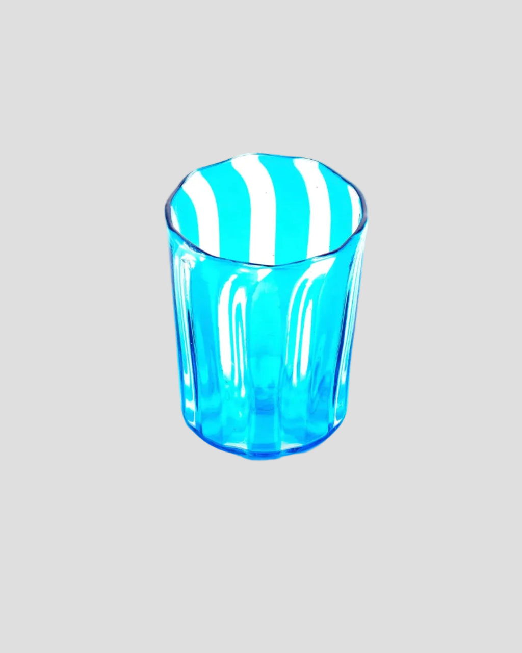A small transparent blue drinking glass with vertical fluted ridges and alternating blue and white diagonal stripes on the rim, shown on a plain white background.