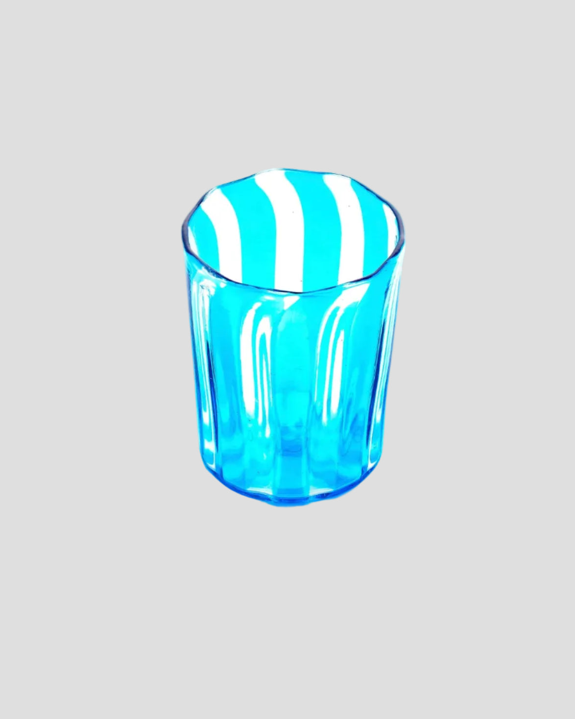 A small transparent blue drinking glass with vertical fluted ridges and alternating blue and white diagonal stripes on the rim, shown on a plain white background.