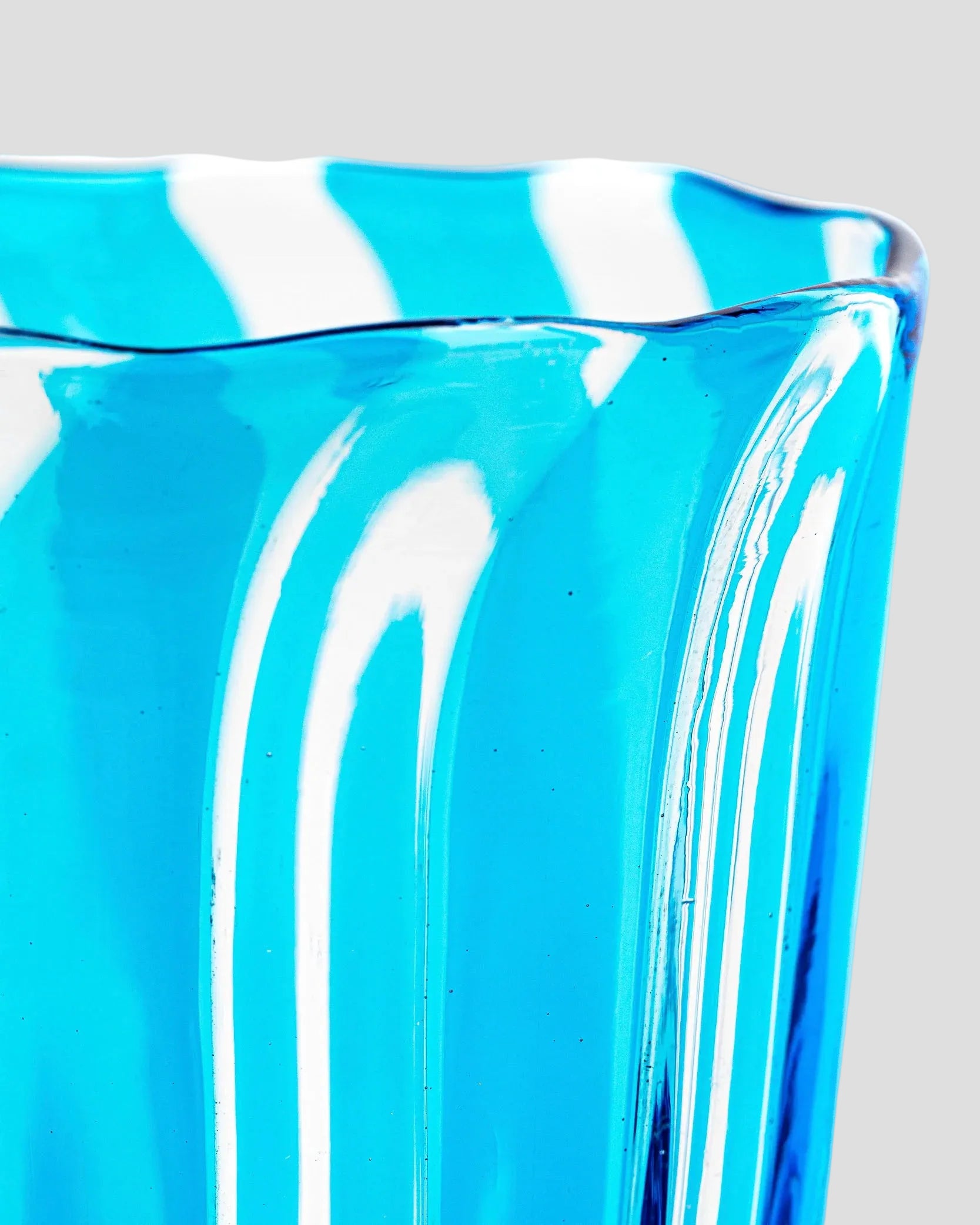 A close-up of a translucent bright blue glass container or vase with a wavy rim, shown against a white background.
