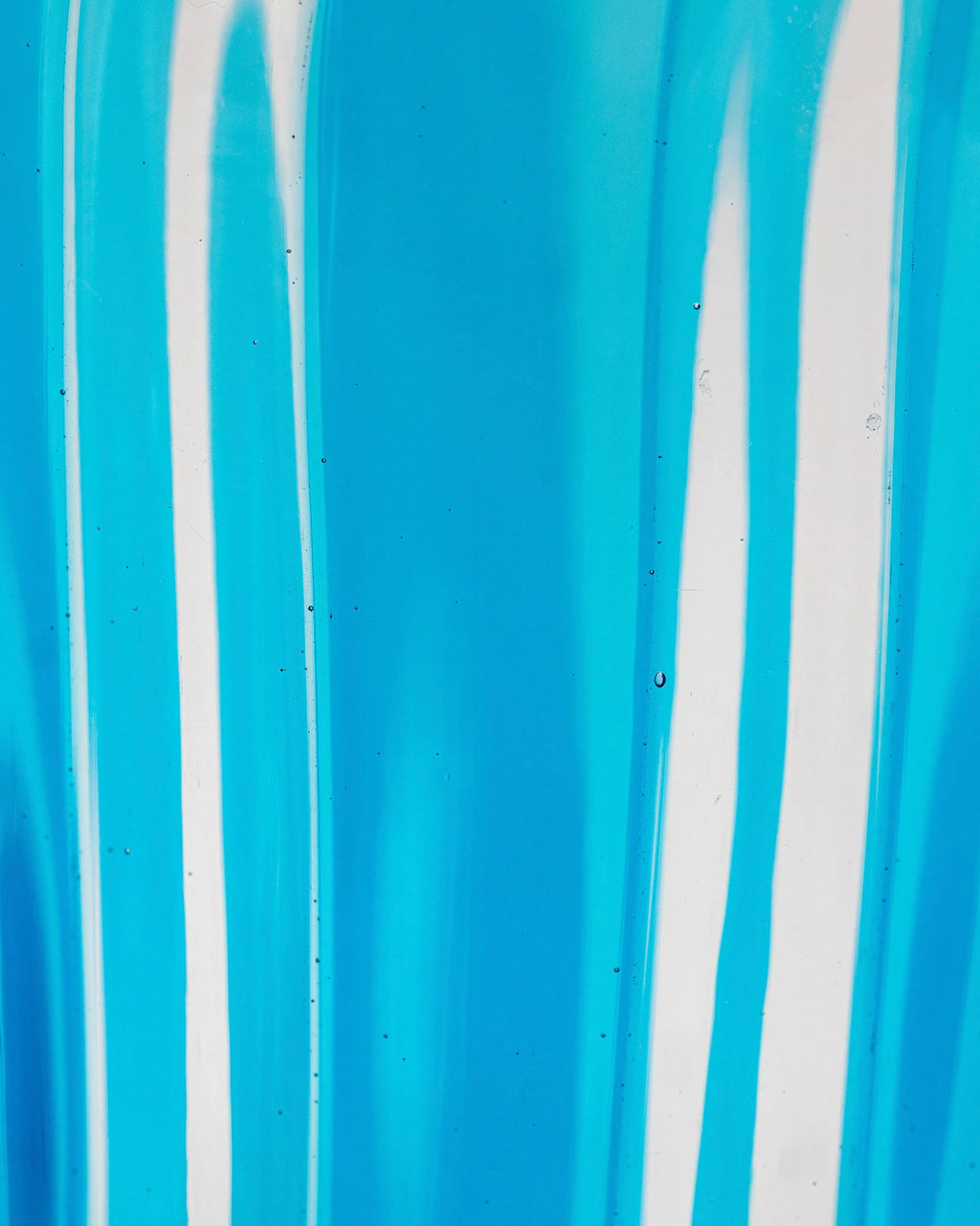 A close-up of a bright blue translucent material with vertical white streaks and a glossy, slightly textured surface.