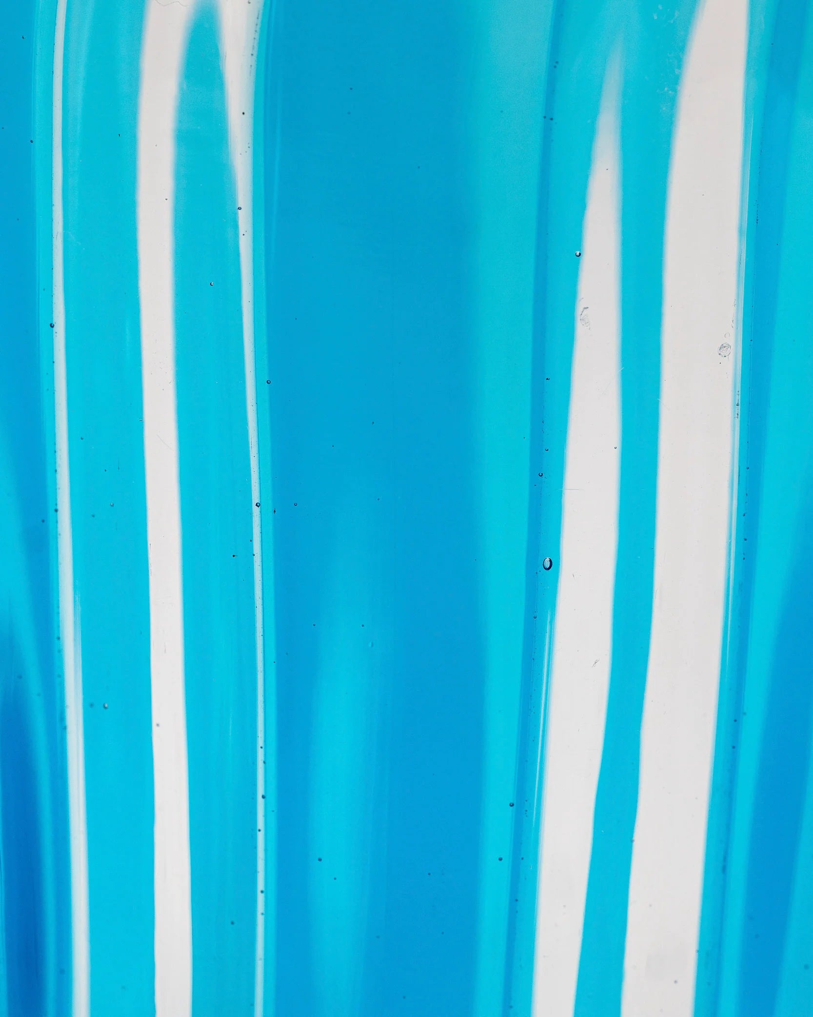 A close-up of a bright blue translucent material with vertical white streaks and a glossy, slightly textured surface.