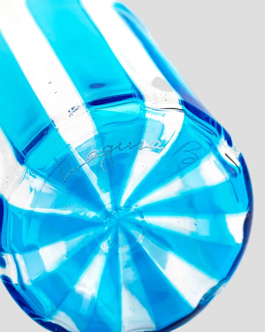 A close-up of a transparent blue glass bottle or container with a faceted circular base and vertical ridges, photographed on a white background.