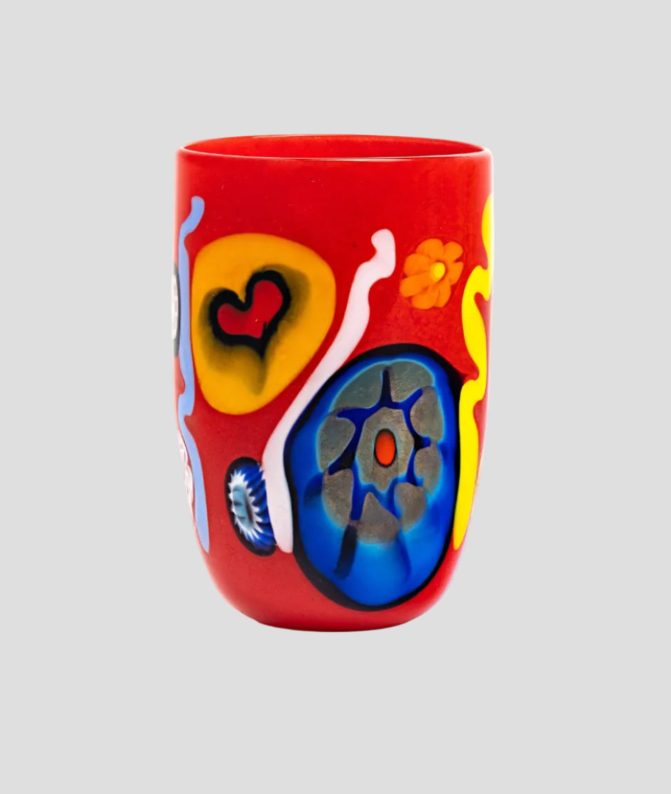 A red glass tumbler decorated with colorful abstract hand-painted motifs including yellow, blue, orange, and white shapes on a white background.