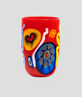 A red glass tumbler decorated with colorful abstract hand-painted motifs including yellow, blue, orange, and white shapes on a white background.