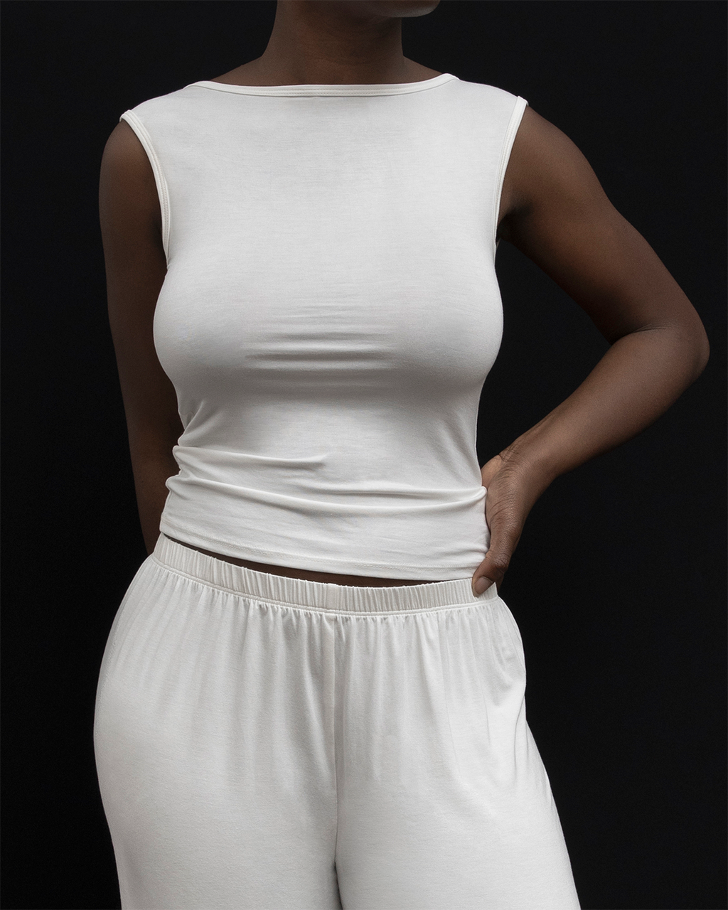 Model wearing Kye Recline Bateau Sleeveless, a white bamboo boat neckline sleeveless tank, paired with white pants.
