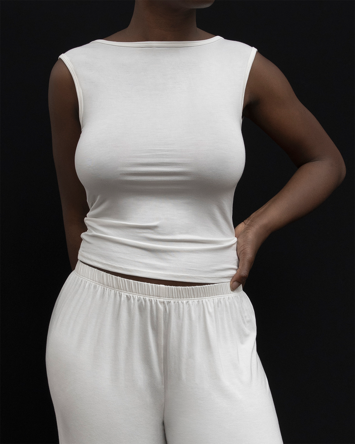 Model wearing Kye Recline Bateau Sleeveless, a white bamboo boat neckline sleeveless tank, paired with white pants.